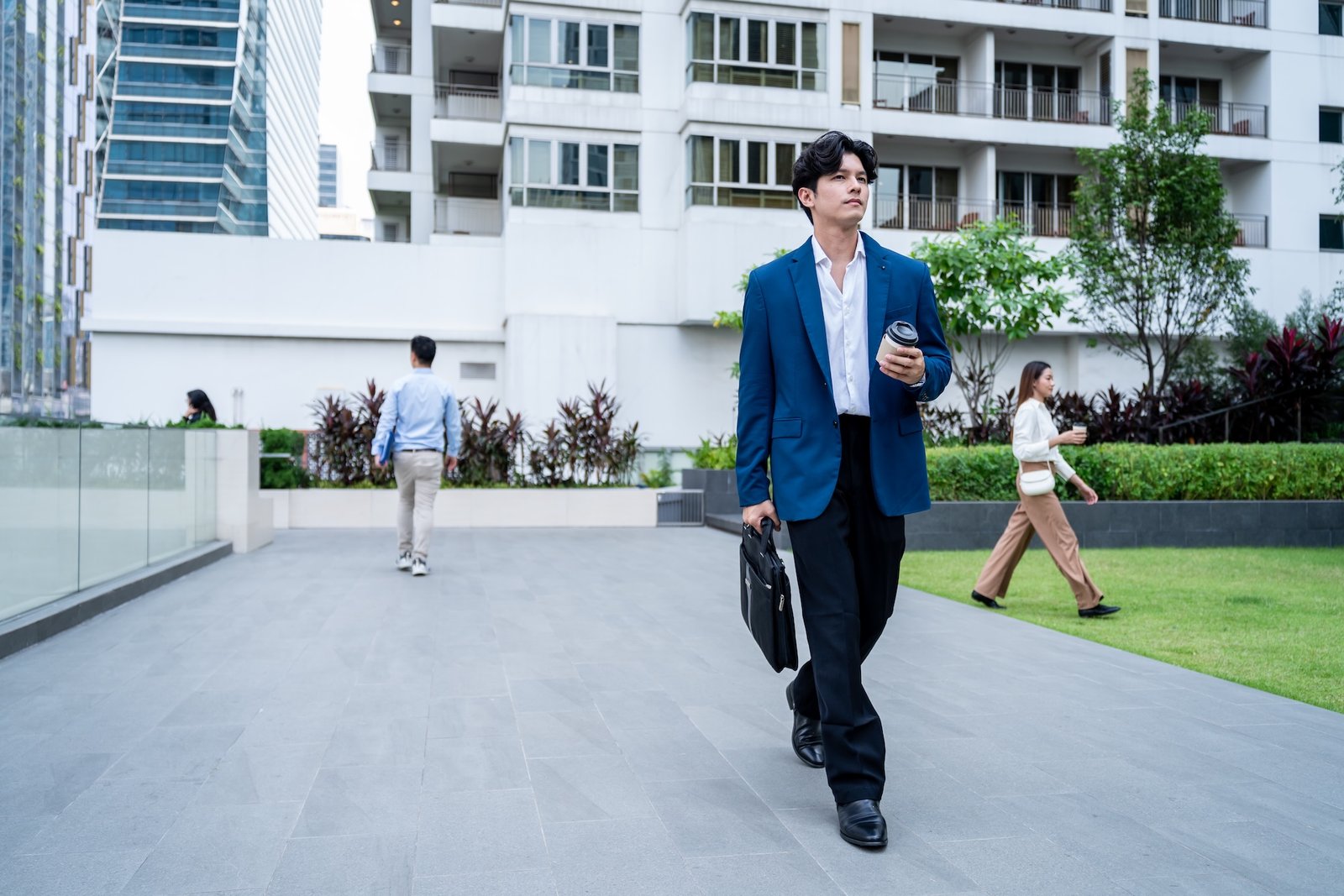 Asian young businessman holding a cup of coffee while walking in city. Attractive handsome male employee worker feeling happy and relax, enjoy morning routine outdoors in urban while going to work.